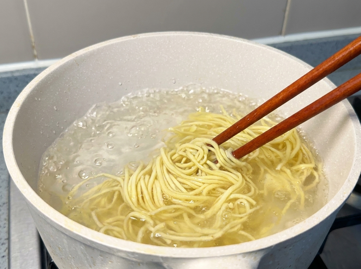 沸騰したお湯から箸で麺を持ち上げている様子。