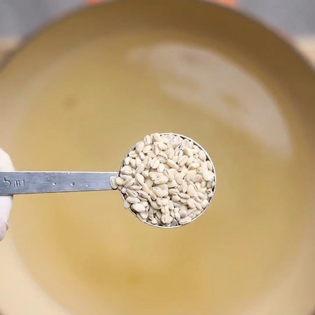 鍋で煮た麦を計量スプーンで持ち上げている様子。