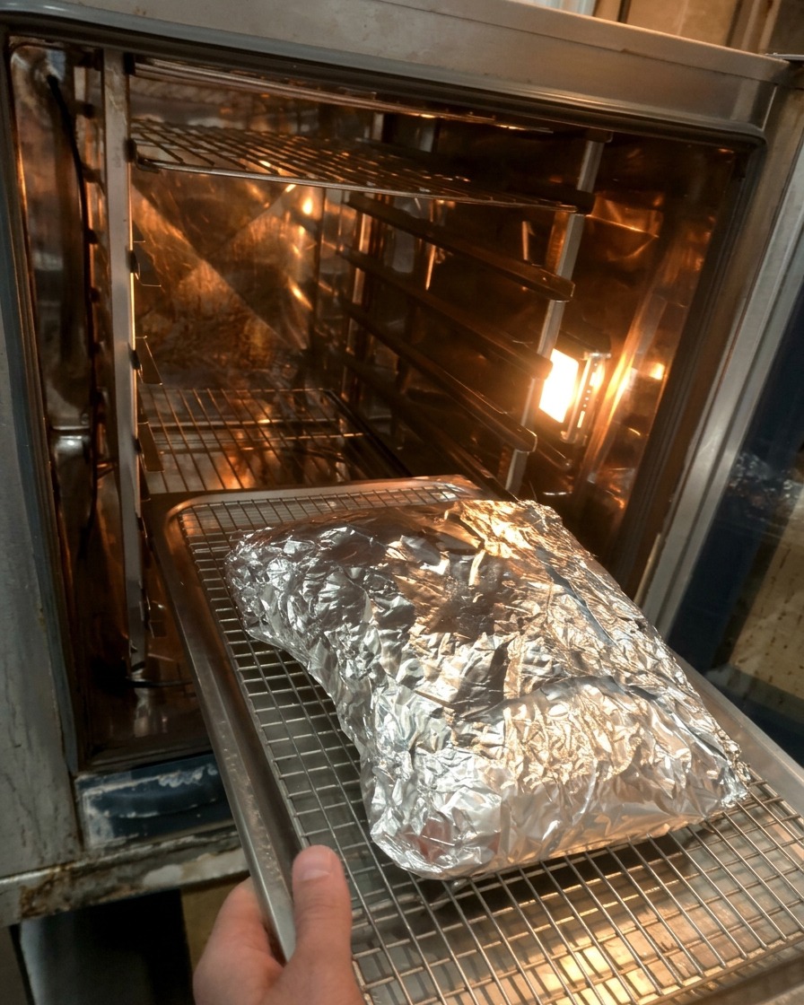 ホイルに包まれた牛肉をオーブンの中の天板にのせる様子。