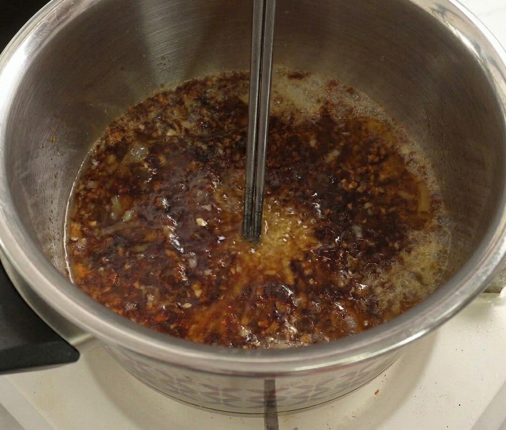 鍋の中でふつふつと煮えるダークなソースをかき混ぜている様子。