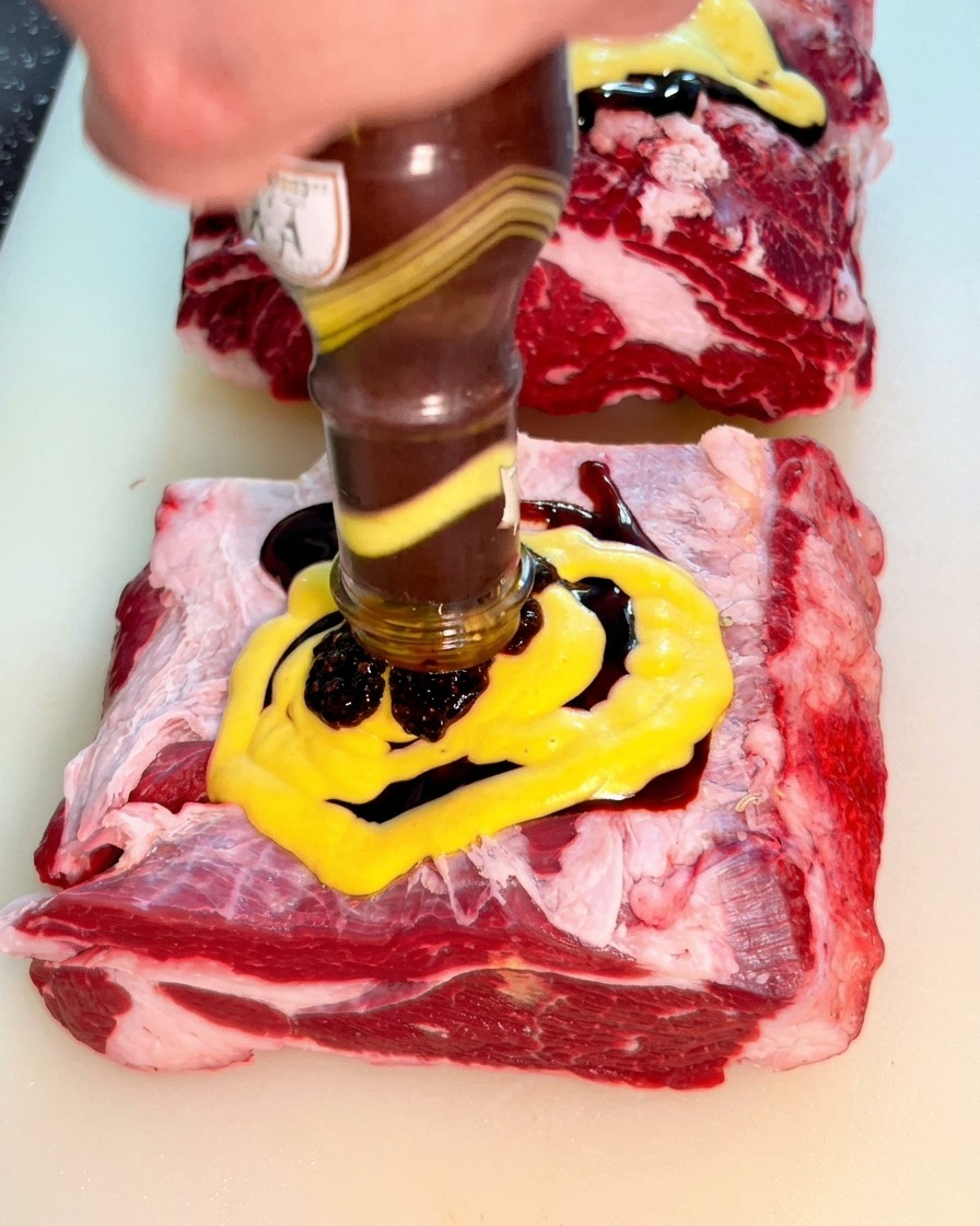 ガラス瓶から、牛肉のマスタード層の上に濃厚な黒胡椒ソースを注いでいる様子。