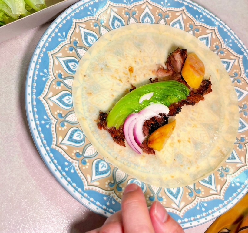 お皿の上のトルティーヤに、スライスした肉、アボカド、赤玉ねぎが盛り付けられている様子。