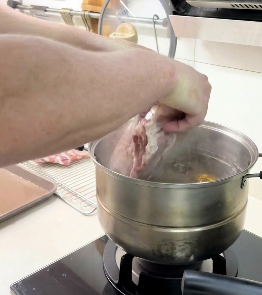 大きなリブの塊を、沸騰した鍋の中に慎重に入れている様子。