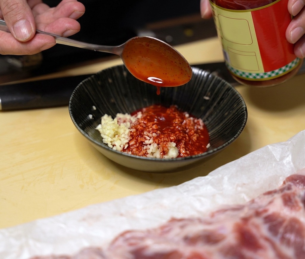 刻んだにんにくが入った黒いボウルに、鮮やかな赤色の南乳の汁を加えている様子。