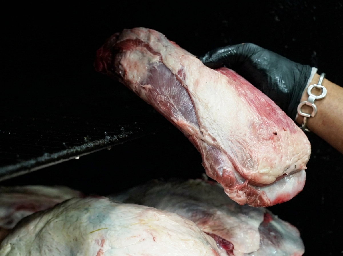 黒い手袋をはめた手が、大きな生の牛肉をブラックスモーカーの網の上に置いている様子