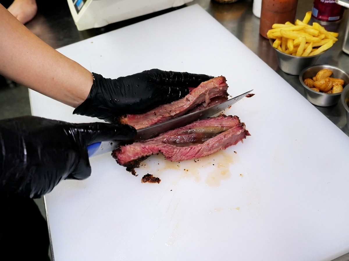 白いまな板の上で、肉厚のスモークビーフリブをナイフでカットし、完璧なピンク色の断面を見せている様子