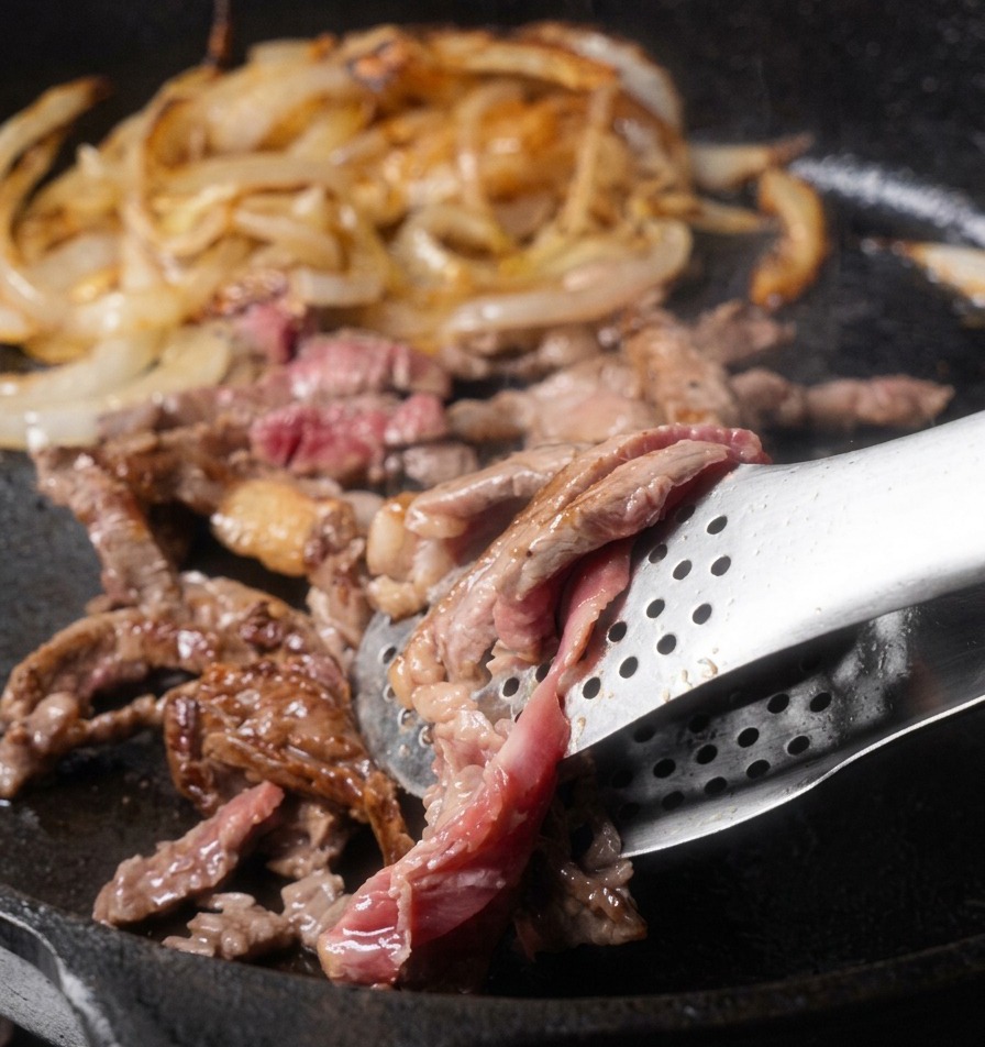 トングで肉を裏返しながら炒め、赤身から美味しそうな茶色に変わっていくリブアイスライスの様子。