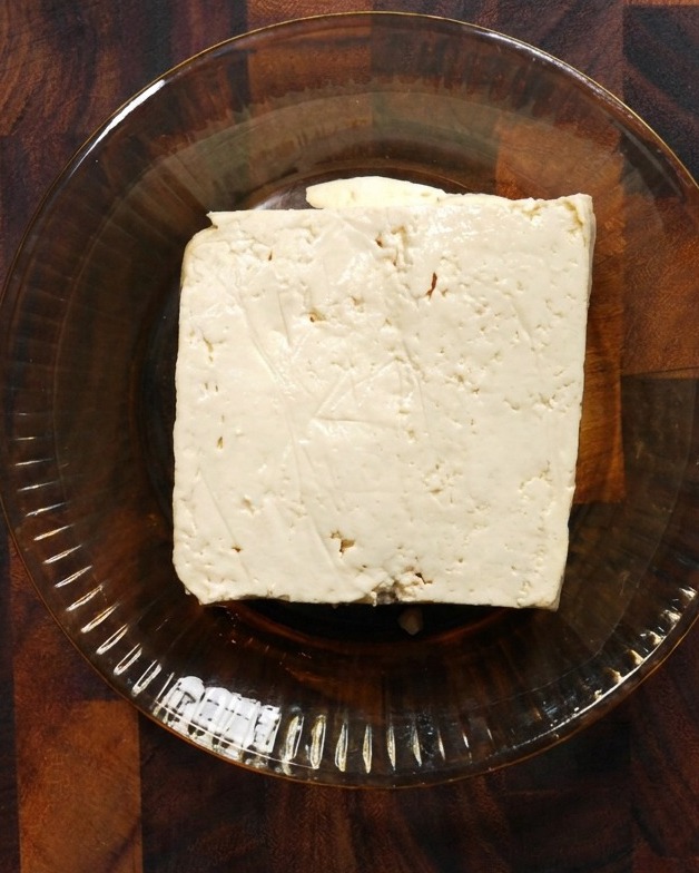 木のテーブルの上の浅いガラスボウルに入った絹ごし豆腐。