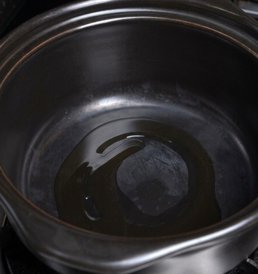 加熱された黒い鍋の底で少量の油が熱されている様子。