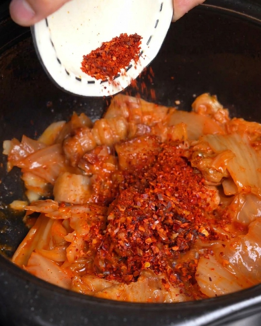 豚肉とキムチを炒めている鍋に赤い粉唐辛子を加えている様子。