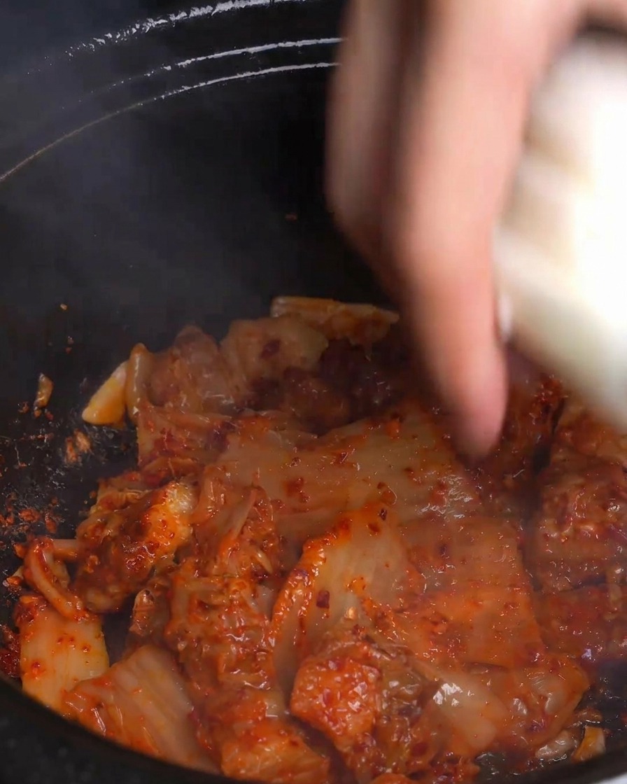 キムチと豚肉が炒められている熱々の鍋に、厚切りの玉ねぎを加えている様子。