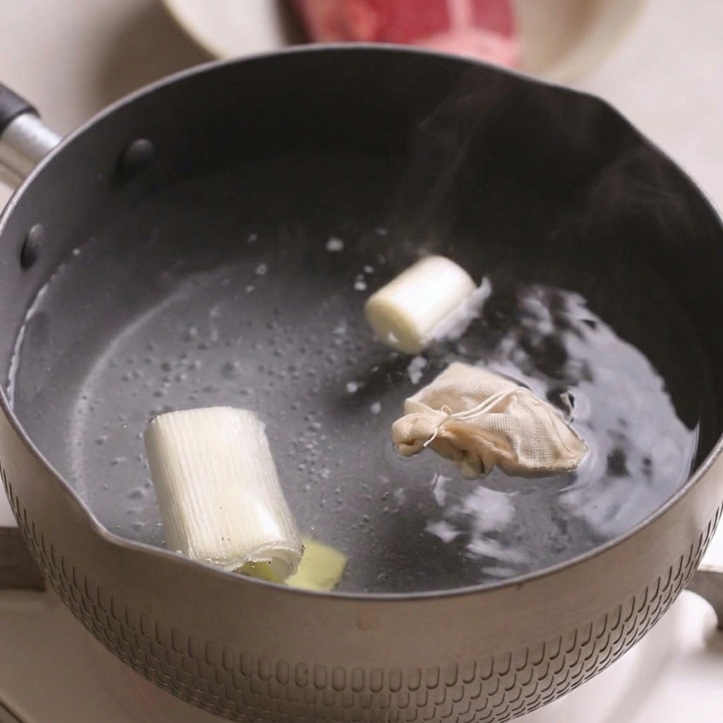 長ねぎ、生姜の薄切り、スパイスバッグを入れた鍋で牛肉をゆでている様子。