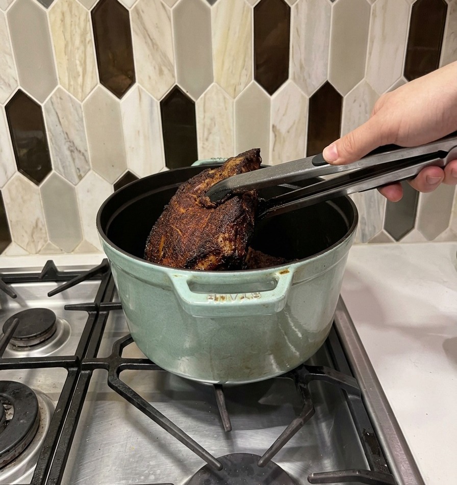 トングを使い、焼き色のついた肉を薄緑色の鋳物ホーロー鍋に移している様子。