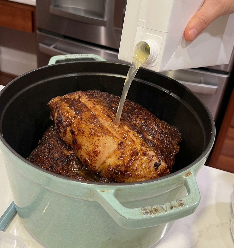 肉が入った鍋に、パックからチキンストックを注いでいる様子。