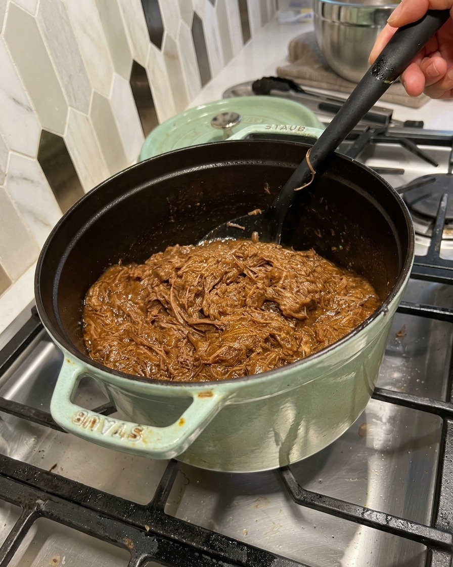 ほぐした肉を鍋に戻し、ヘラを使って濃厚なBBQソースと混ぜ合わせている様子。