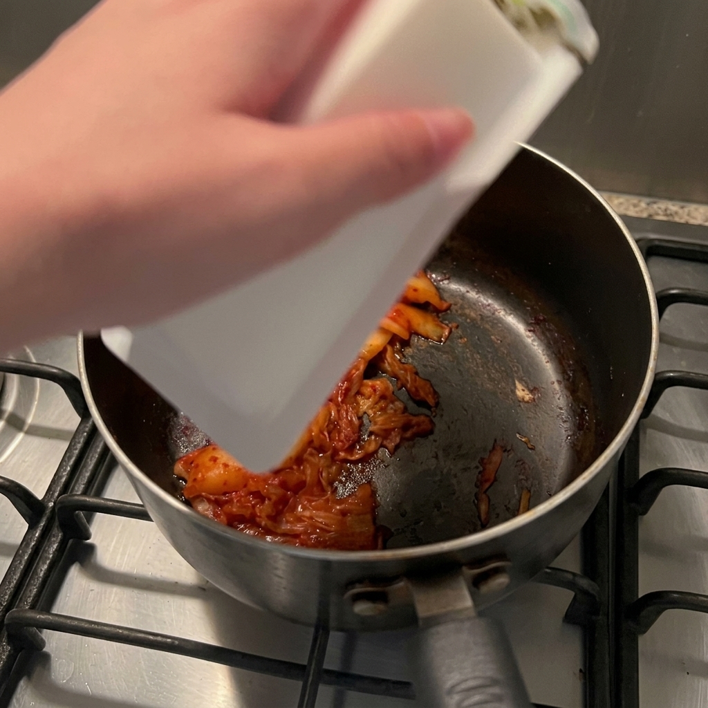 炒めたキムチが入った鍋に、パックから絹ごし豆腐を滑らせて入れている様子