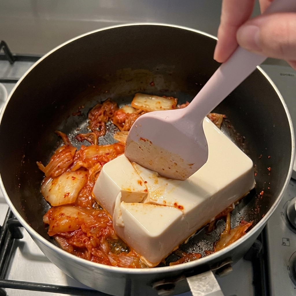 鍋の中でシリコンヘラを使い、白い豆腐を大きくカットしている様子