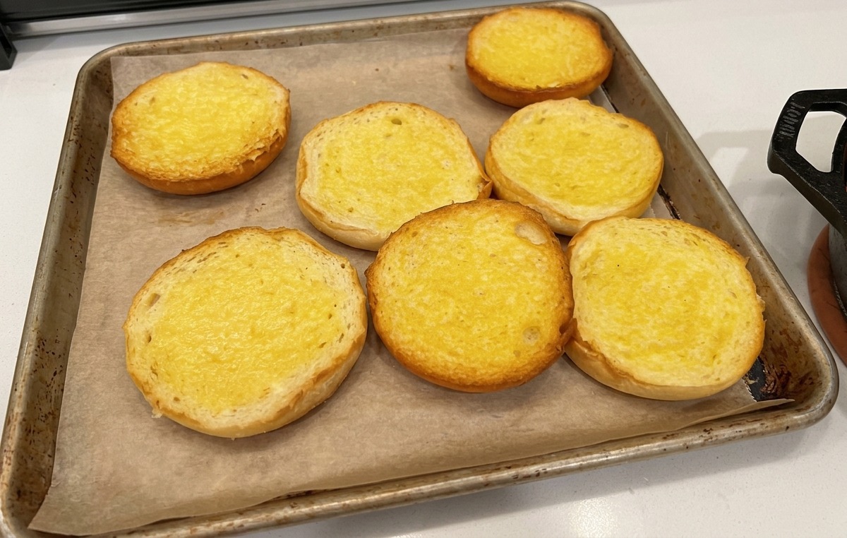 天板に並べられた、断面にバターを塗ったハンバーガー用バンズの様子。