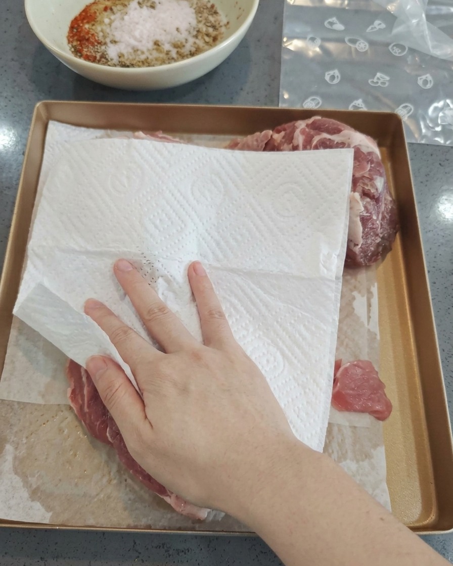 トレーに置いた生の豚肉の水分を、キッチンペーパーで丁寧に拭き取っている様子。