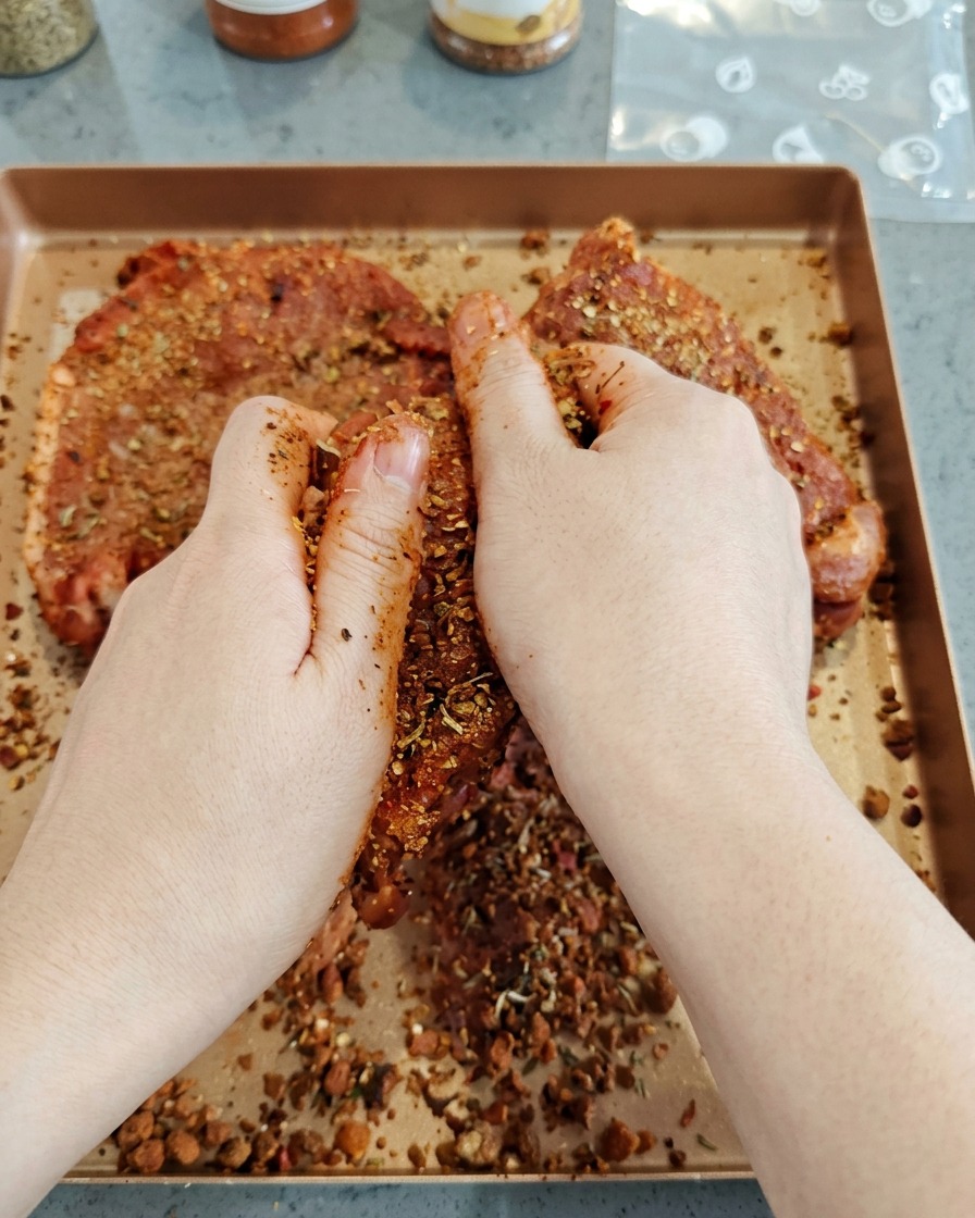 生の豚肉の大きな塊に、手でダークカラーのスパイスをしっかり揉み込んでいる様子。