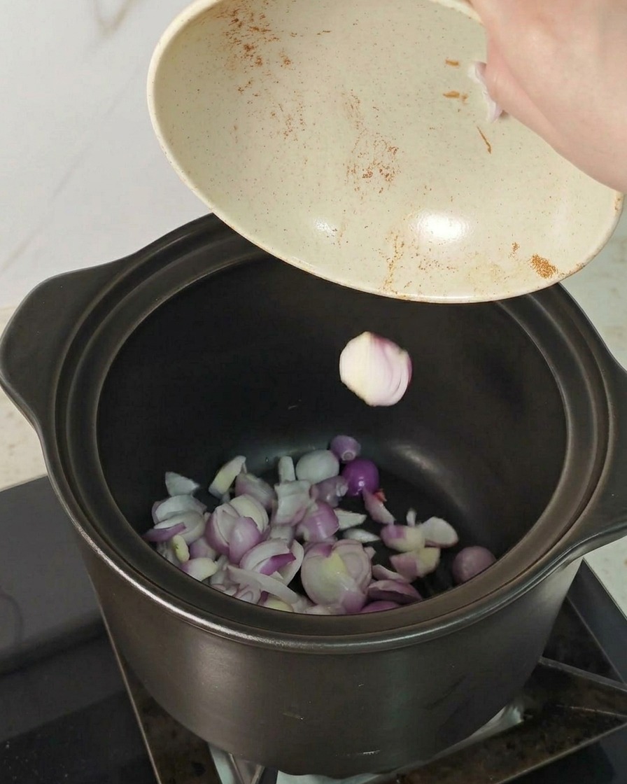 煮込み用の厚手の鍋の底に、スライスした赤エシャロットを敷き詰めている様子。