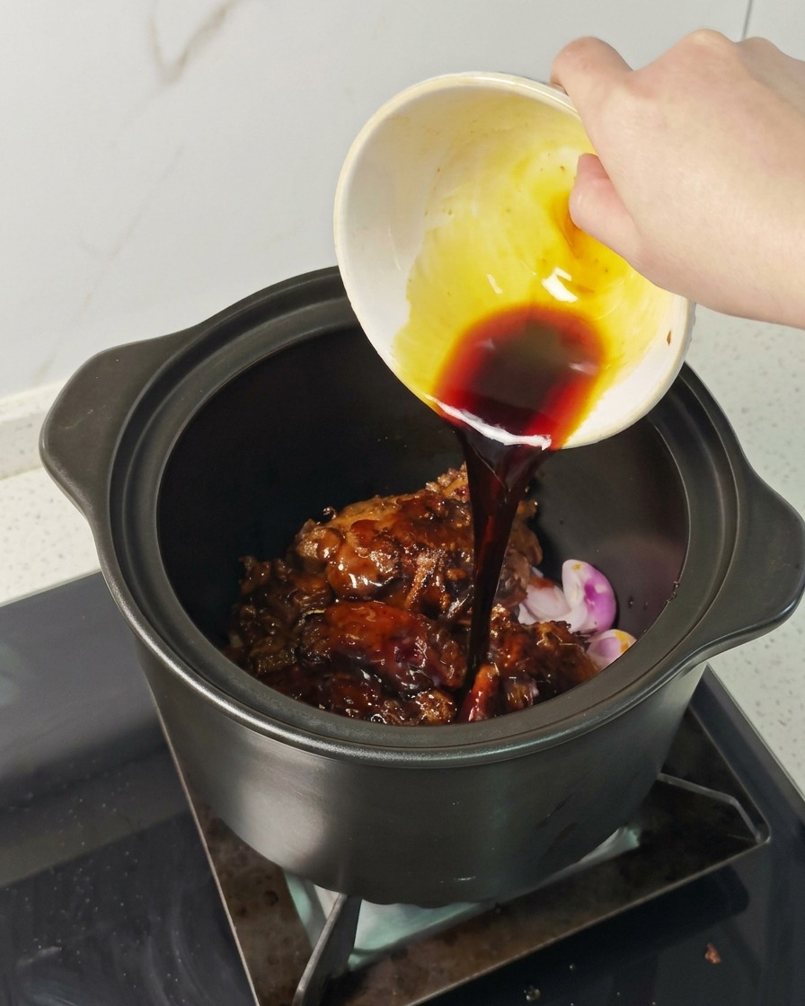 鍋の中の肉の上から、濃い色の煮込み用ソースを回しかけている様子。