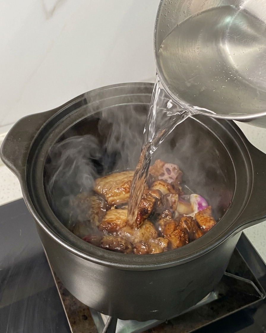 肉とエシャロットが入った鍋に、ケトルから湯気の立つ熱湯を注いでいる様子。