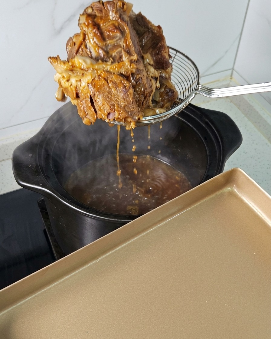 湯気が上がる鍋から、網じゃくしを使って柔らかくなった大きな豚肉を引き上げている様子。