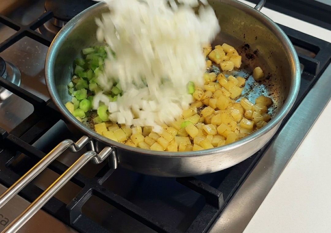 じゃがいもとセロリが入ったフライパンに玉ねぎを加える様子。