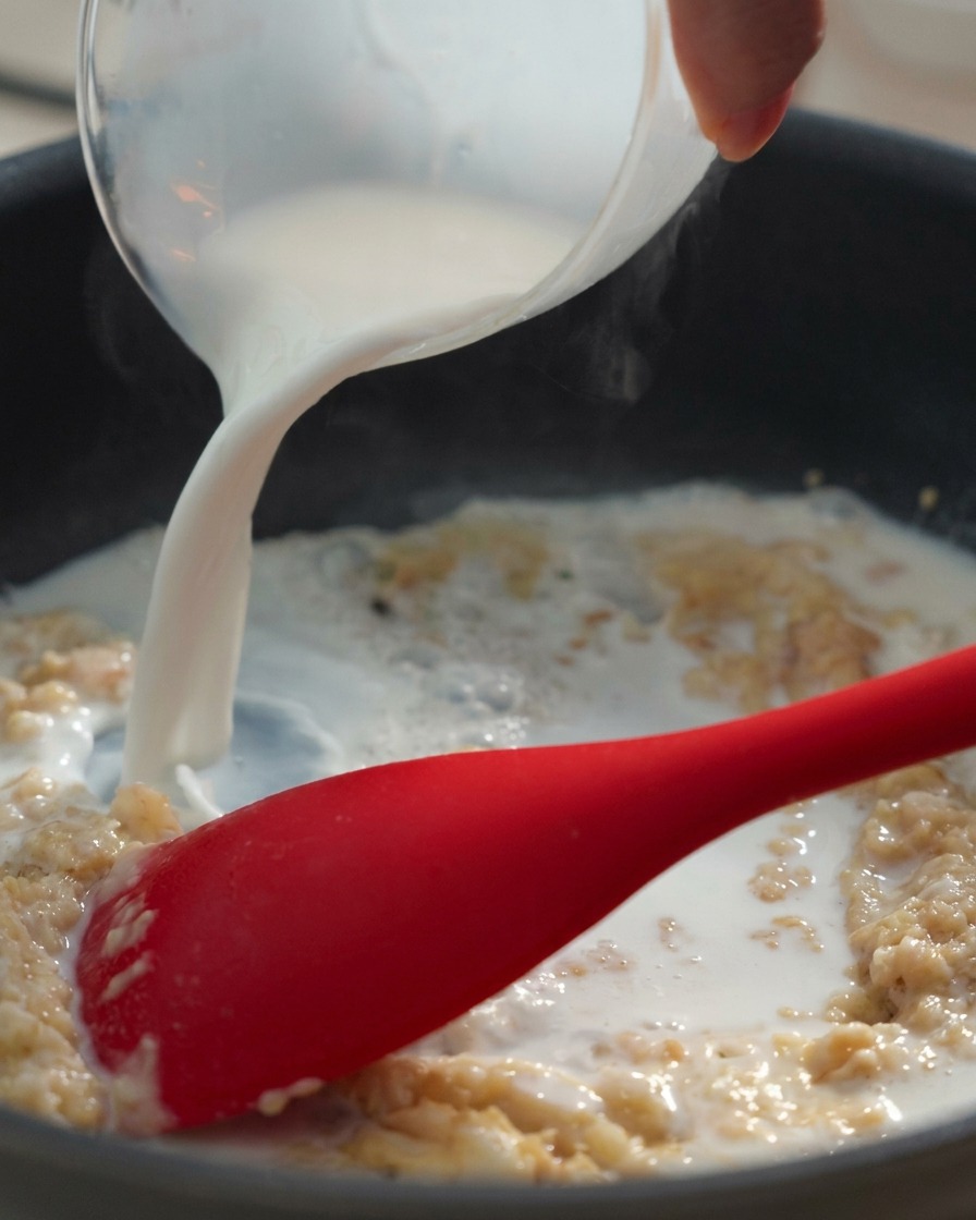 計量カップから牛乳を注ぎ、バターと小麦粉のペーストと混ぜ合わせている様子。