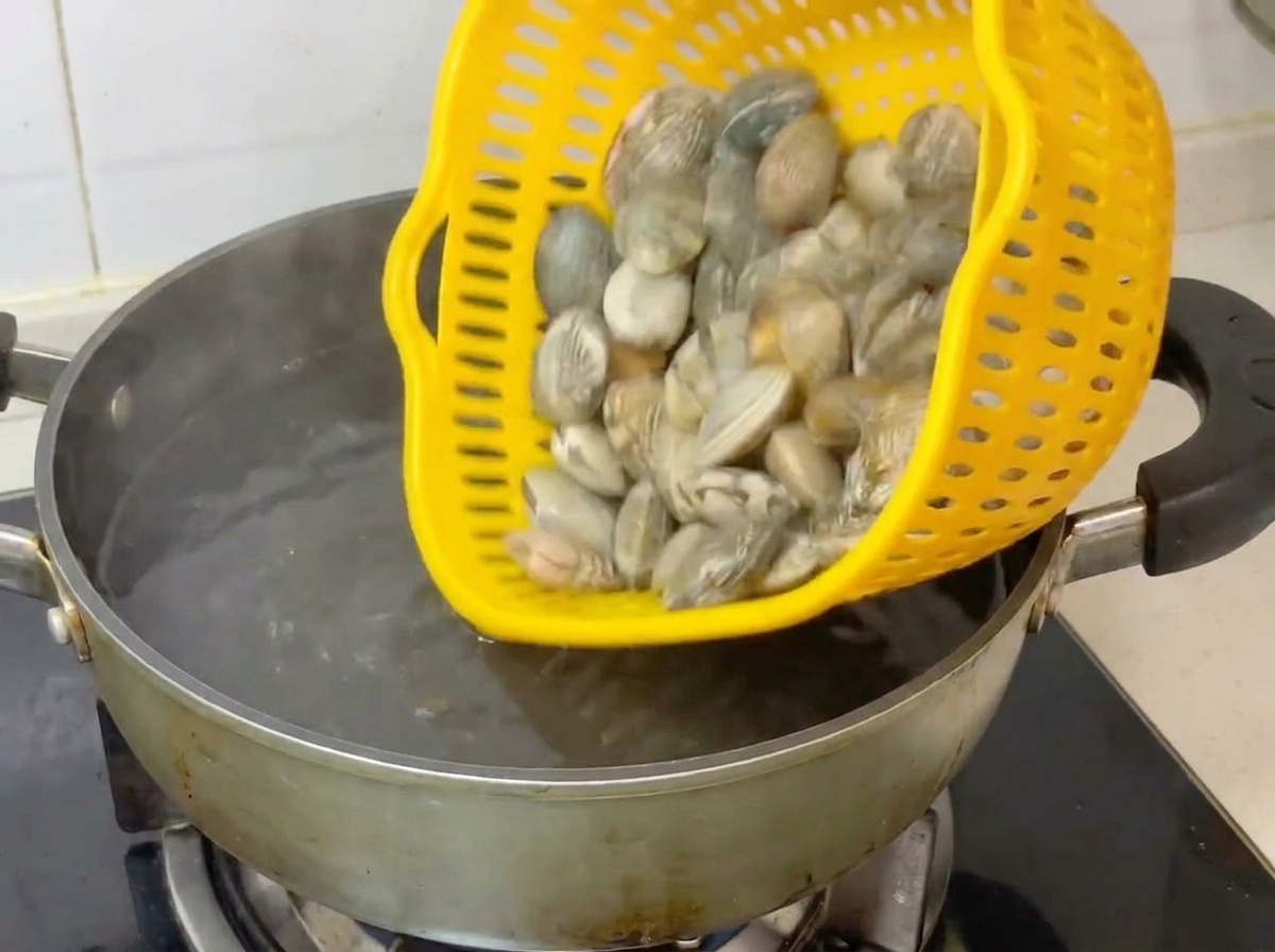 黄色いザルから沸騰したお湯の入った鍋にあさりを移している様子