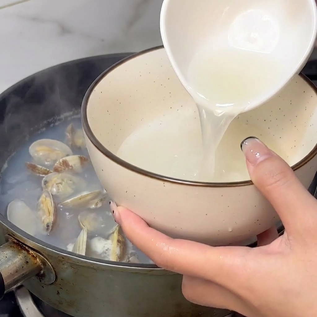 調理したあさりの鍋から、白いお玉で蒸し汁をすくい取っている様子