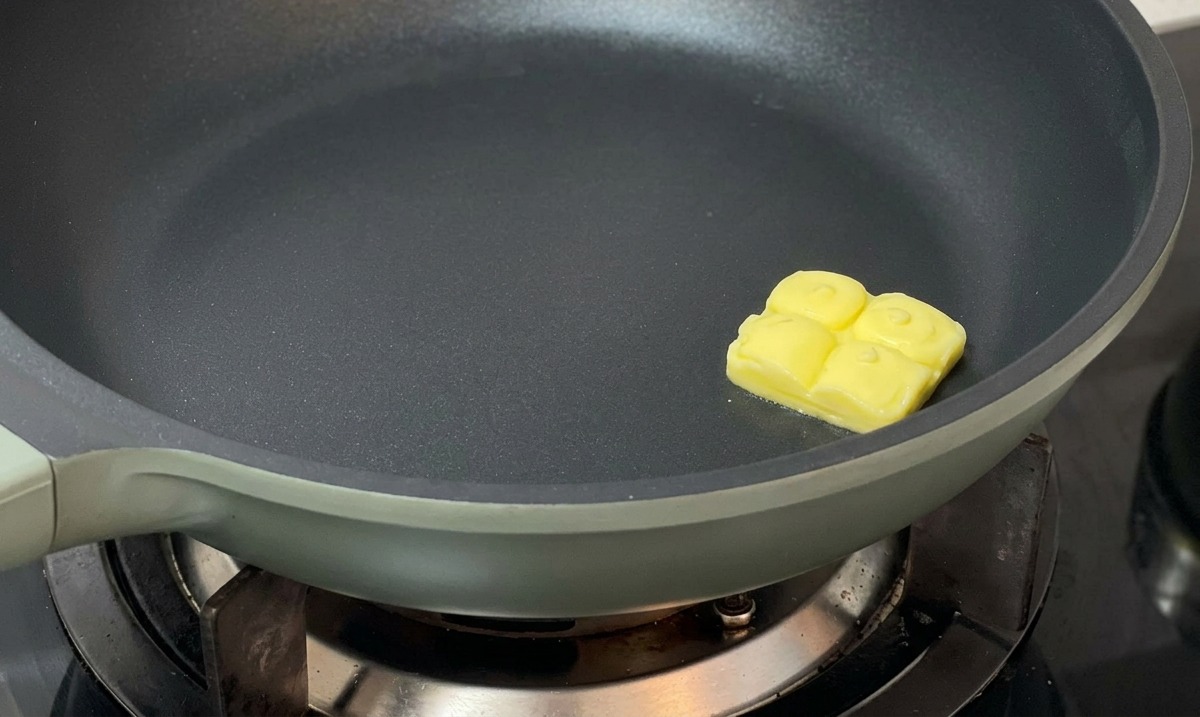 暗い色のフライパンの中央で、角切りのバターがゆっくりと溶けている様子