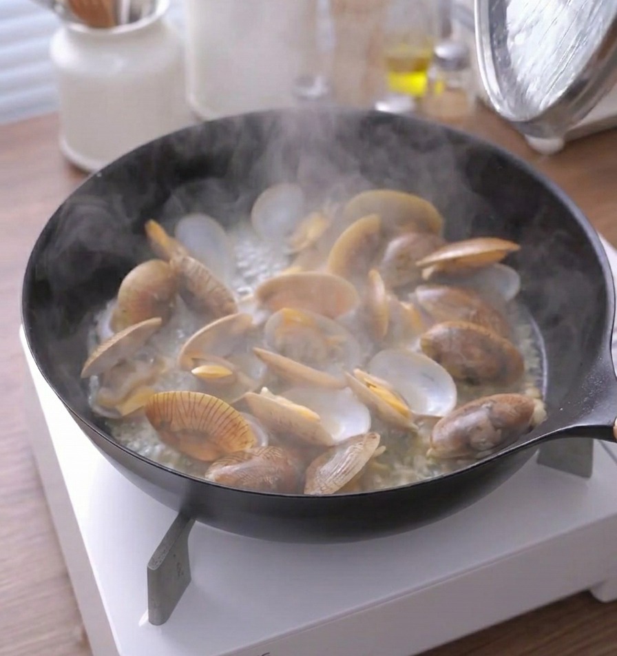 口の開いたあさりのフライパンから大量の湯気が立ち上っている様子。