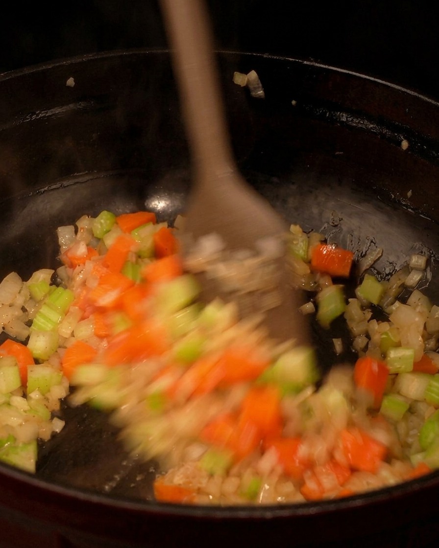 炒めた香味野菜の中に角切りのじゃがいもを入れ、木べらで混ぜ合わせている様子。