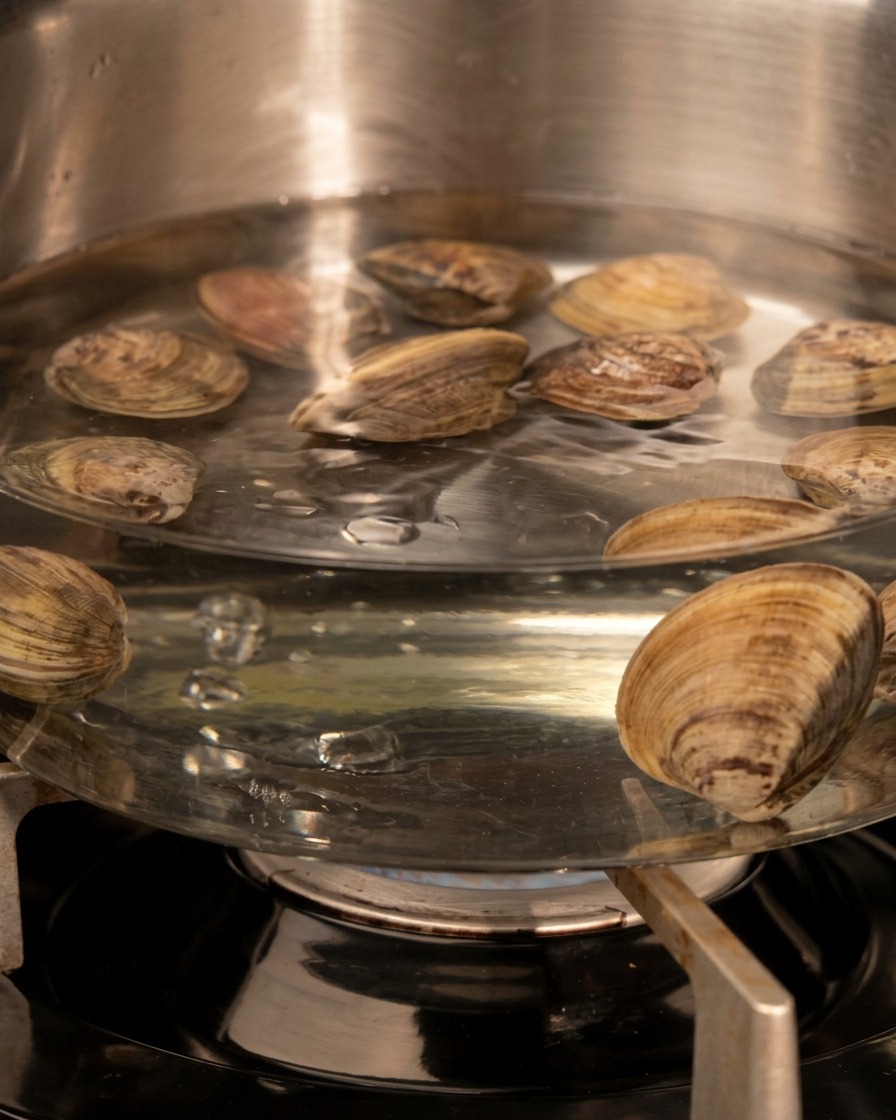 沸騰したお湯の中に、殻を閉じた新鮮なあさりが入れられる様子。