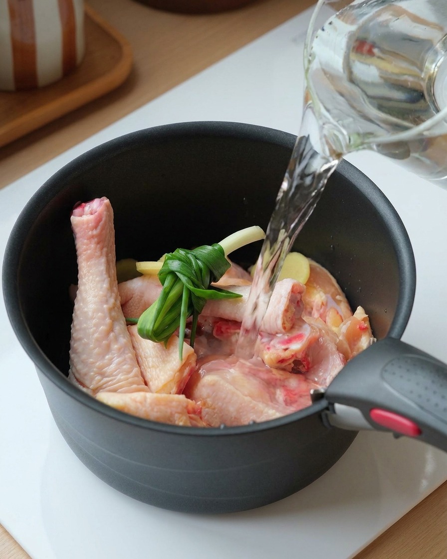 鶏肉、結んだネギ、スライスした生姜が入った鍋に水を注いでいる様子。