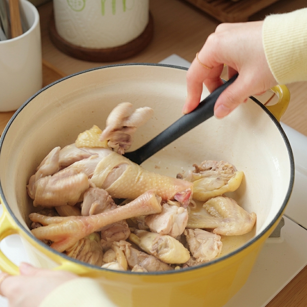 黄色の鍋の中で、スパチュラを使って下茹でした鶏肉を炒めている様子。