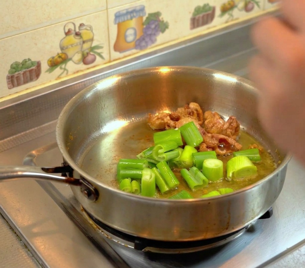 フライパンの鶏油で、ざく切りにした長ねぎの葉を揚げ焼きにしている様子。