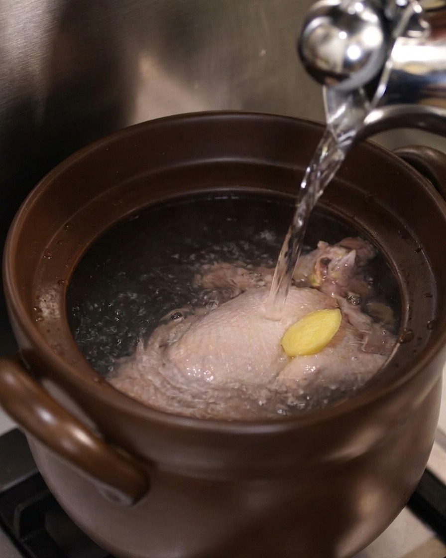 土鍋の中の鶏肉と生姜に、ケトルから熱湯を注いでいる様子。