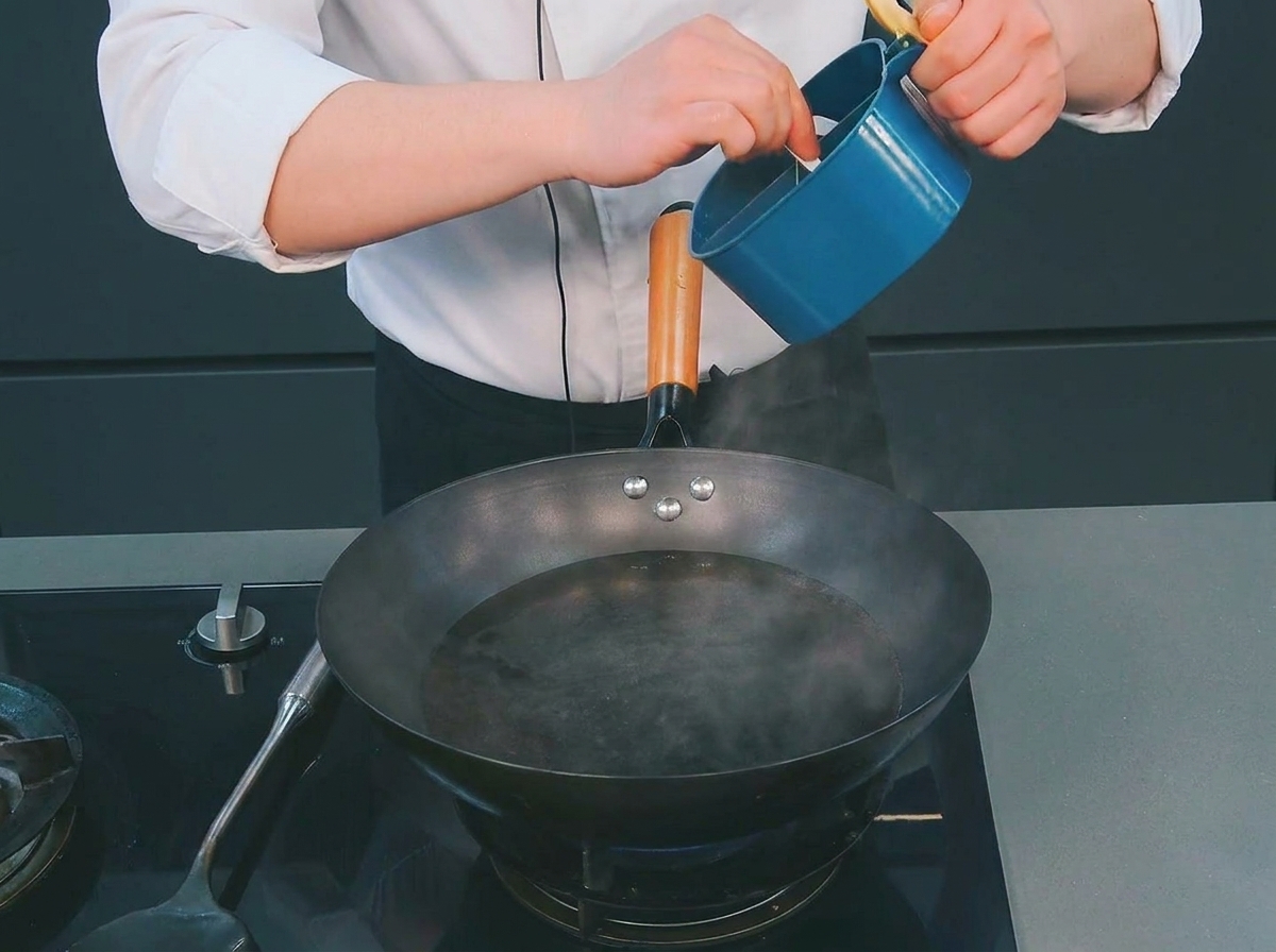 蒸気が上がる中華鍋の熱湯に、シェフが青い容器から塩を加えている様子。