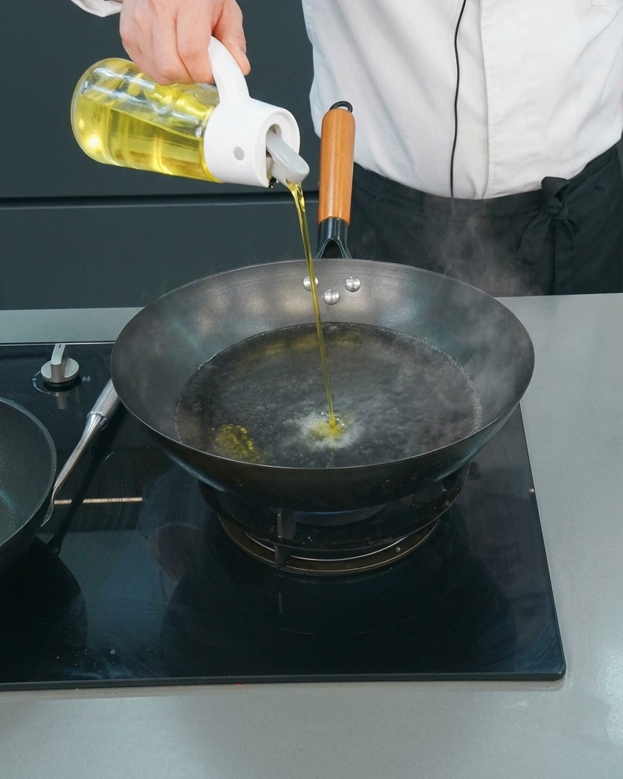 沸騰したお湯が入った中華鍋に、オイル差しから油を注いでいる様子。
