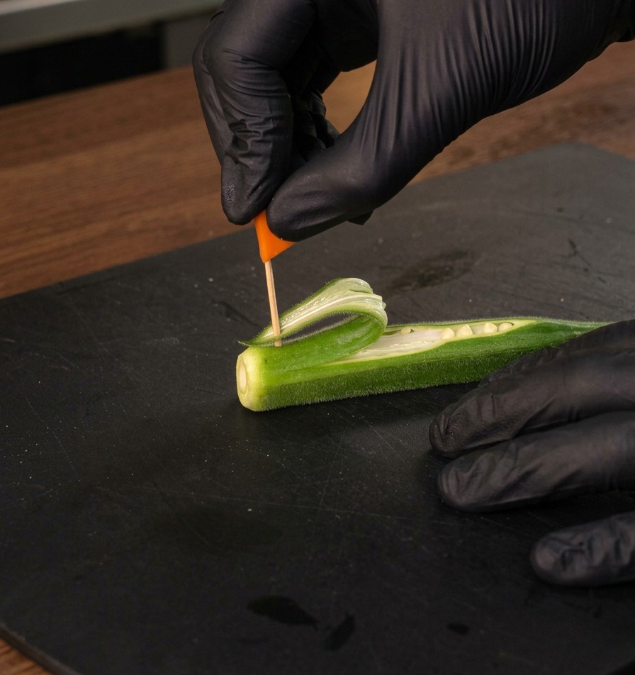 オクラで作った帆の頂点に、人参で作った小さなオレンジ色の旗を刺す様子。