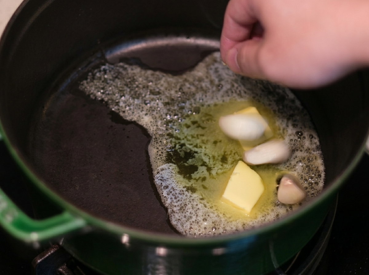 緑色の鋳物鍋の中で溶けたバターにみじん切りのにんにくを加えている様子。