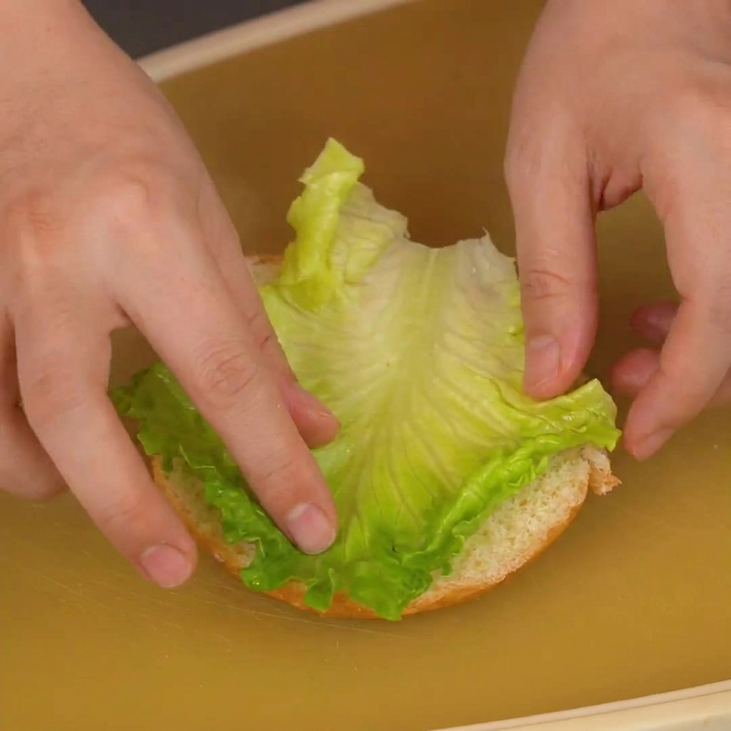 カットした下のバンズに、鮮やかな緑色のレタスを乗せている手元。