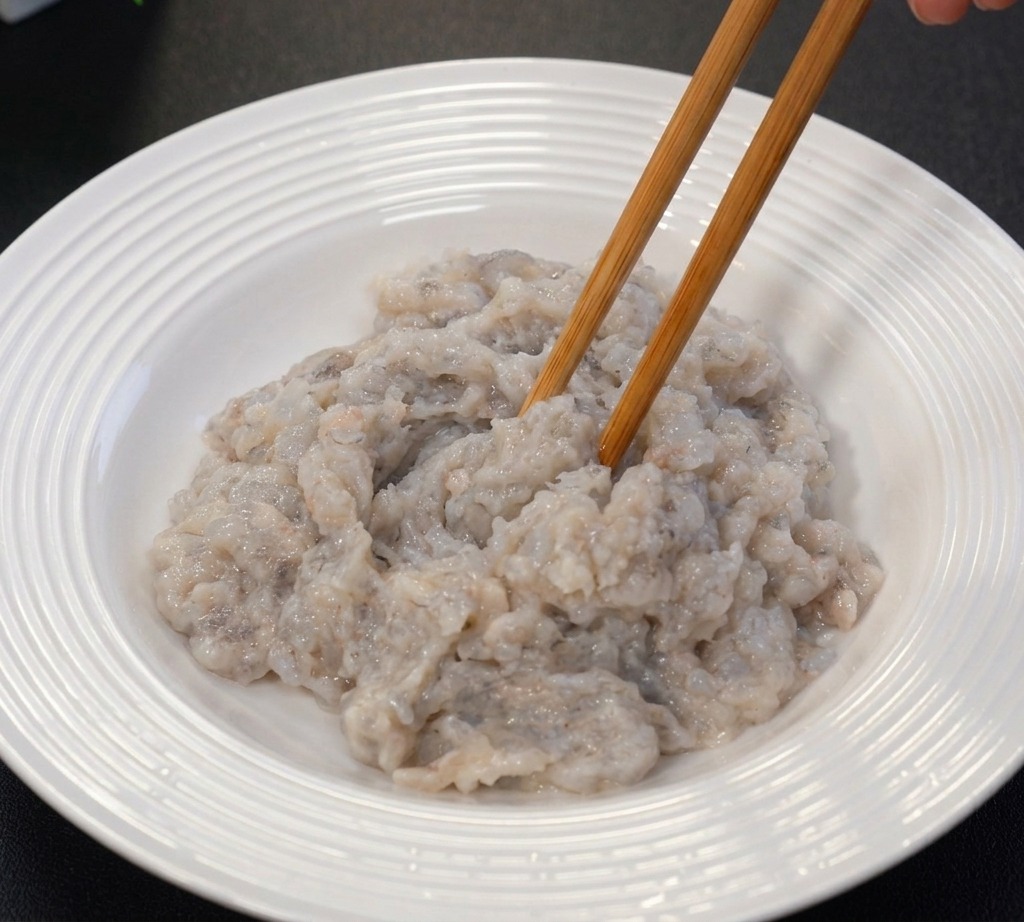 白いボウルの中で、グレーの海老のすり身を菜箸を使って練り上げている様子。