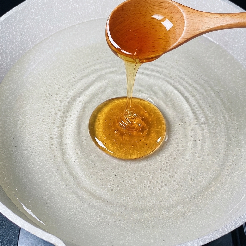 沸騰したお湯に木製のスプーンで黄金色の油を注いでいる様子。