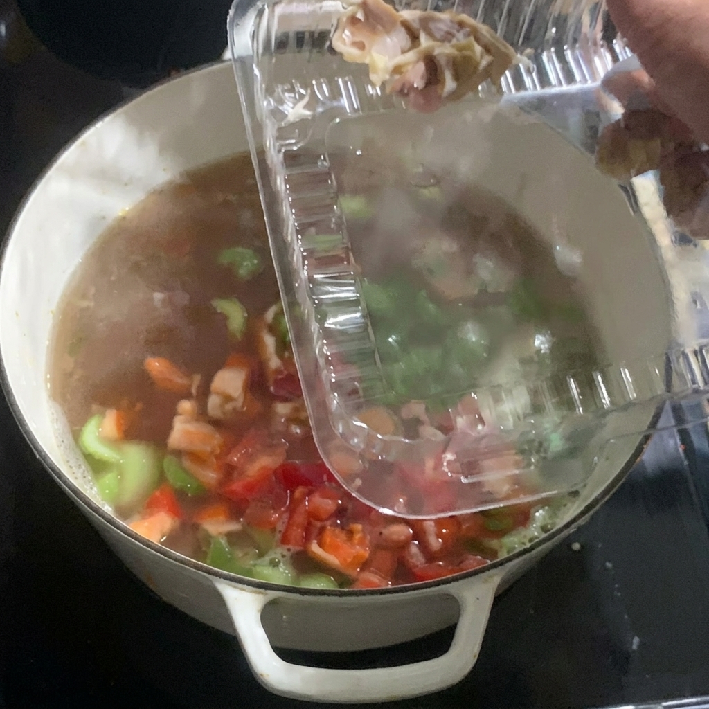 煮込んでいる野菜とスープの中に、プラスチック容器から加熱済みの鶏肉を加えている様子。