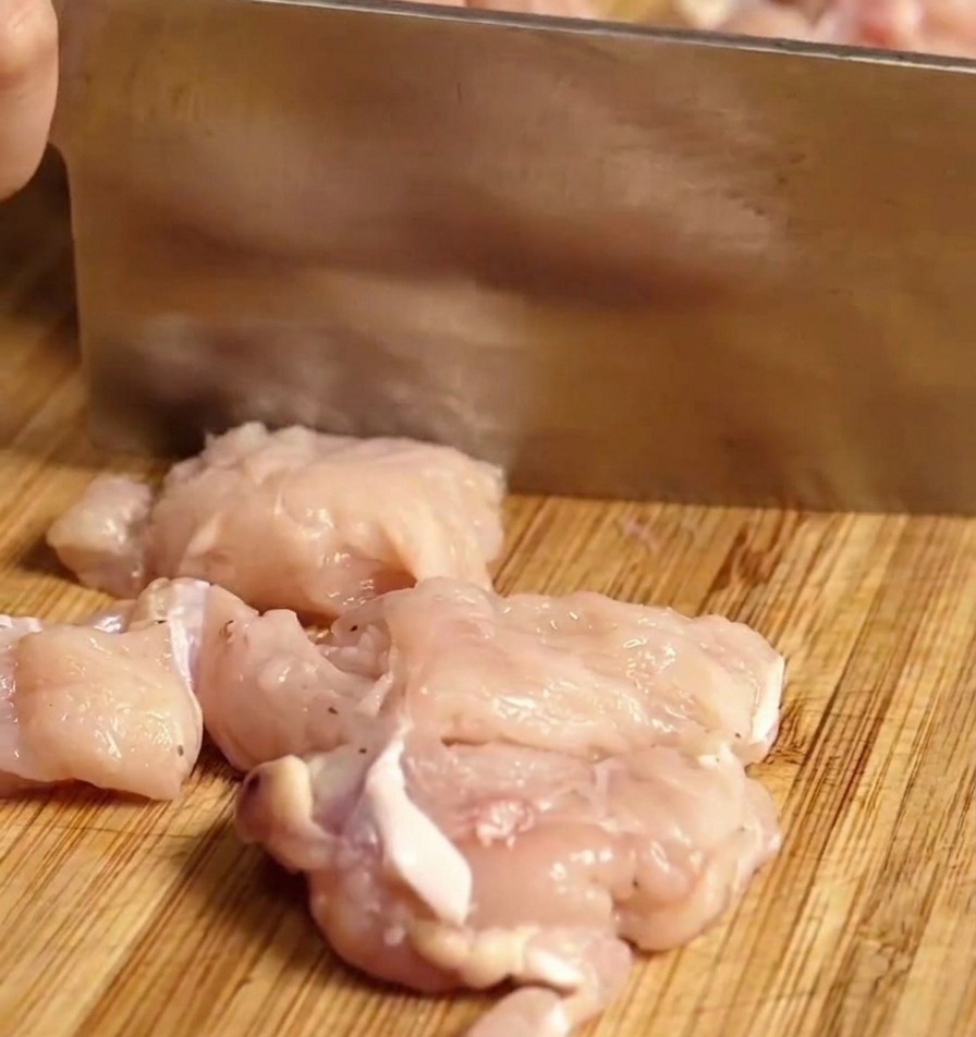 まな板の上で生の鶏むね肉を一口大の角切りにしている様子。