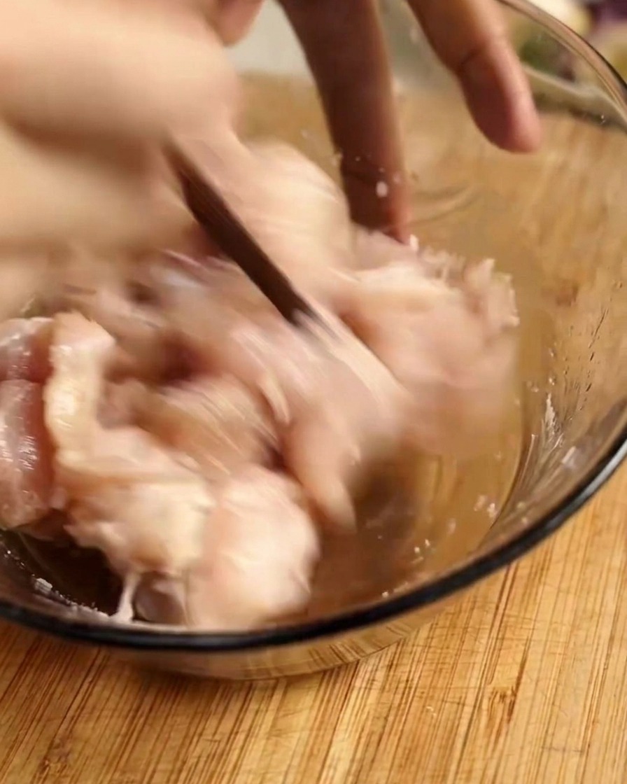 ガラスボウルの中で、鶏肉に下味の調味料を加えて箸で手早く混ぜ合わせている様子。